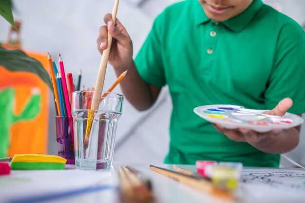 Mão de meninos segurando pincel em copo de água