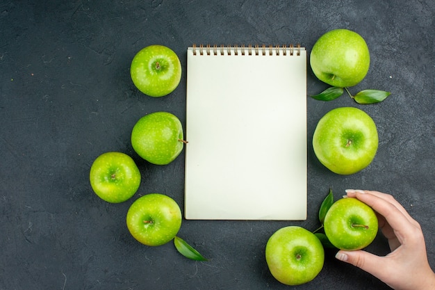 Mão de mulher de maçã verde de caderno de vista superior segurando uma maçã na superfície escura