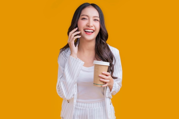 Mão de mulher de negócios asiática inteligente casual usando smartphone segure conversa de negócios de xícara de café sorrindo olhe para a câmera confiante expressão facial alegre estúdio tiro fundo amarelo