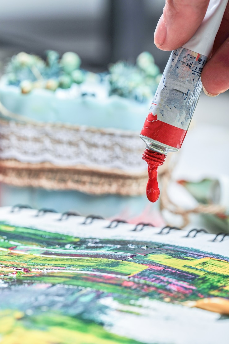 Foto grátis mão de mulher desenhando quadro de pintura com tubos de pintura.