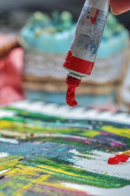 Mão de mulher desenhando quadro de pintura com tubos de pintura.