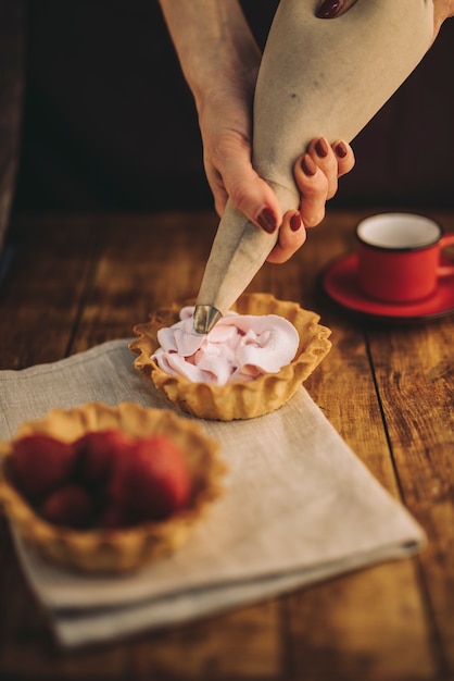 Mão de mulher enchendo o creme de manteiga-de-rosa com saco de confeiteiro na mesa de madeira