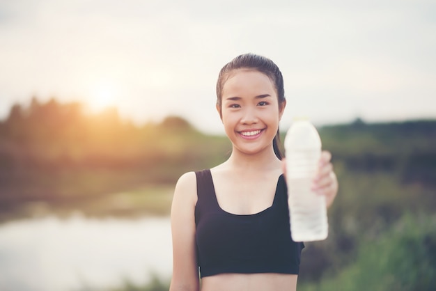 Mão de mulher jovem fitness segurando a garrafa de água após a execução do exercício