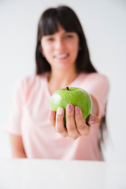 Mão de mulher oferecendo a maçã verde contra o pano de fundo branco