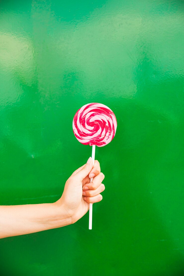 Foto grátis mão de mulher segurando pirulito vermelho e rosa na mão contra fundo verde