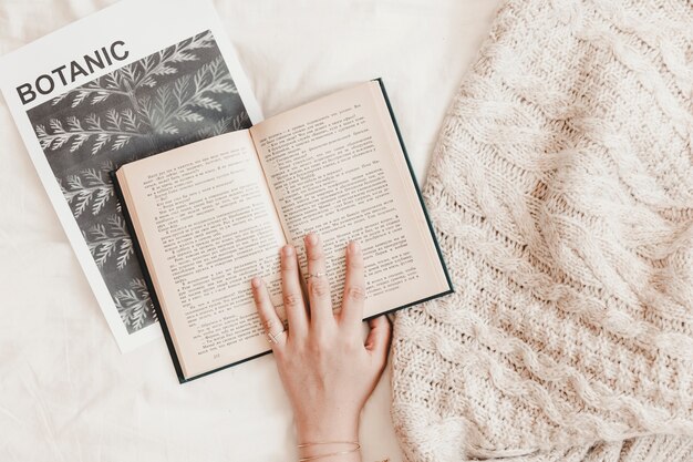 Mão de mulher sendo no livro deitado no banner e cobertor no lençol