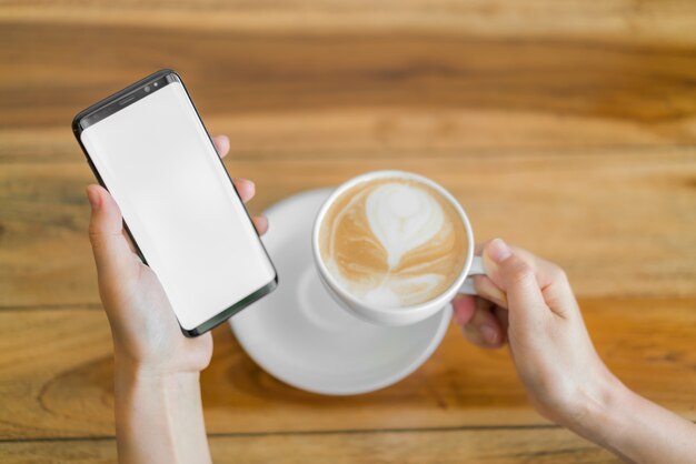 Mão de negócios com o telefone móvel e o café da arte latte.