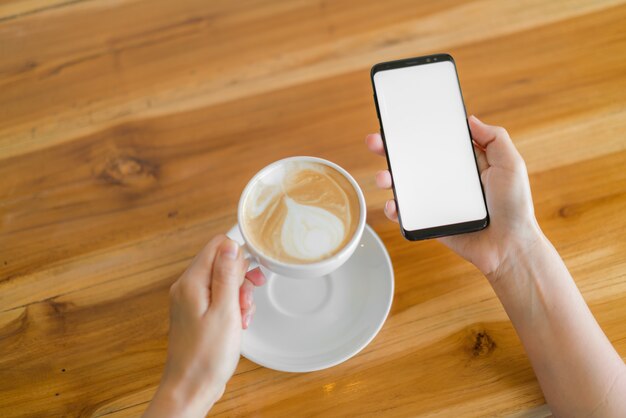 Mão de negócios com o telefone móvel e o café da arte latte.