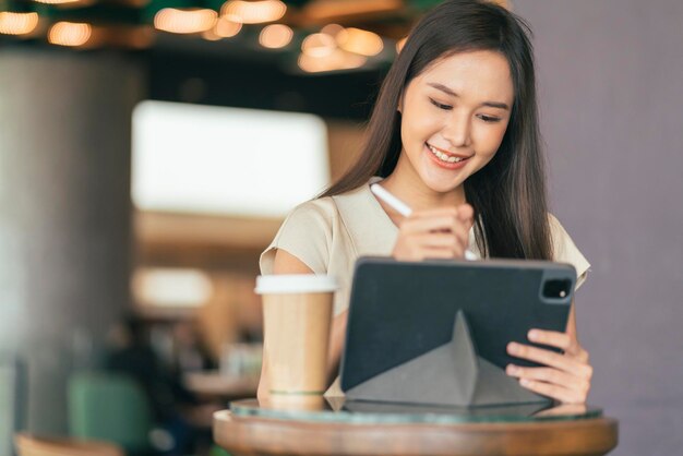 Mão de nômade digital freelancer asiática usando tablet trabalhando remotamente em qualquer lugar de trabalho sente-se no balcão perto do bar fazendo contato com o cliente no exterior com um acordo de sucesso pacífico sorridente alegre