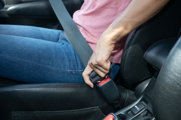 Mão de uma mulher apertando o cinto de segurança no carro, imagem recortada de uma mulher sentada no carro e colocando o cinto de segurança, conceito de condução segura.