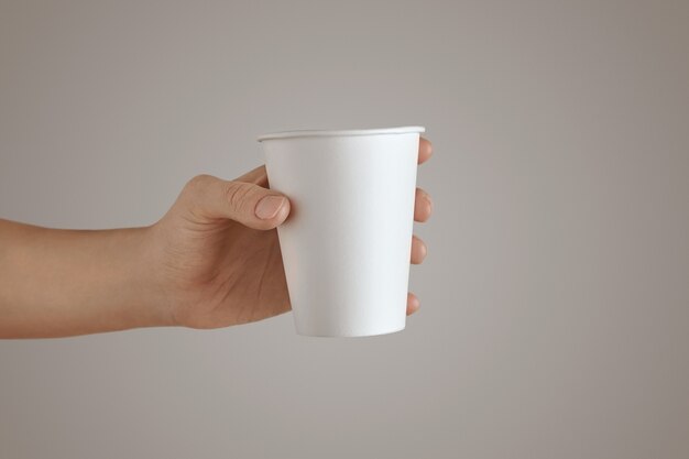 Mão de uma mulher segura a vista lateral do copo de papel em branco vazio, isolado, irreconhecível