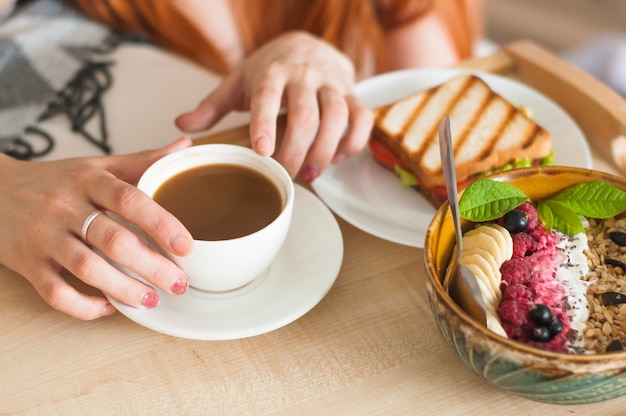 Mão de uma mulher segurando a xícara de chá com sanduíche e café da manhã de aveia