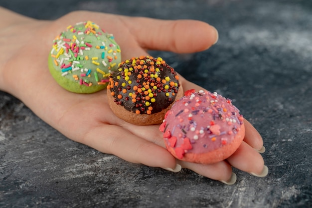 Mão de uma mulher segurando donuts doces coloridos com granulado.