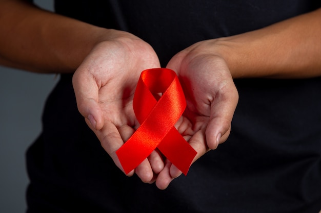 Mão de uma mulher segurando o conceito de conscientização de HIV fita vermelha Dia Mundial da Aids e Dia Mundial da Saúde Sexual.