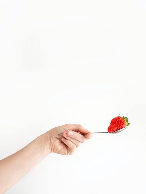 Mão de uma pessoa segurando uma colher com um morango em uma superfície branca