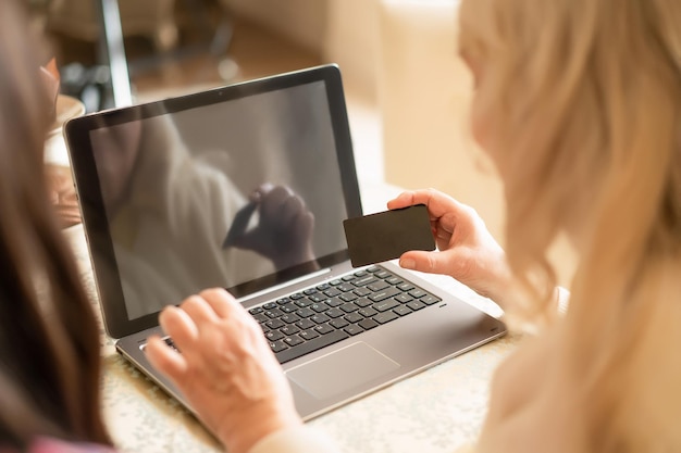 Mão de uma senhora idosa segurando um cartão do banco e inserindo o código PIN para verificar as finanças