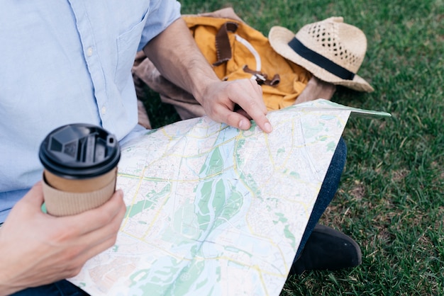 Mão do homem, segurando a xícara de café descartável e pesquisando o destino no mapa enquanto está sentado no parque
