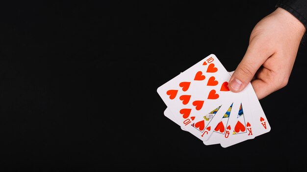 Mão do jogador de poker com royal flush coração em fundo preto