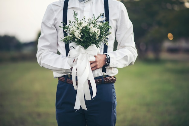 Mão do noivo segurando flor de amor no dia do casamento