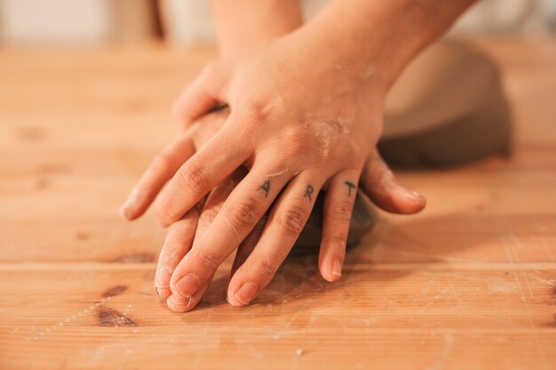 Mão do oleiro feminino amassar a argila na superfície de madeira