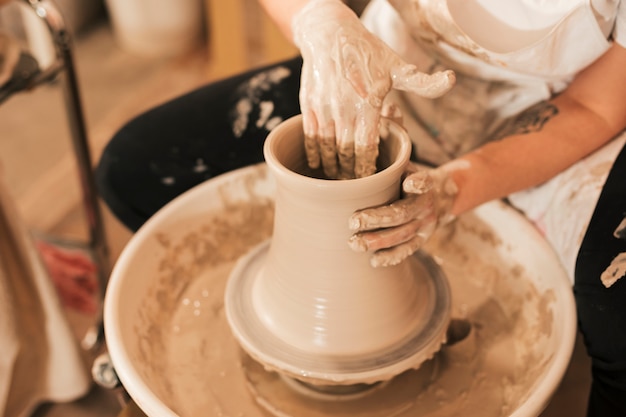 Mão do oleiro feminino fazendo pote de cerâmica com barro na roda de oleiro