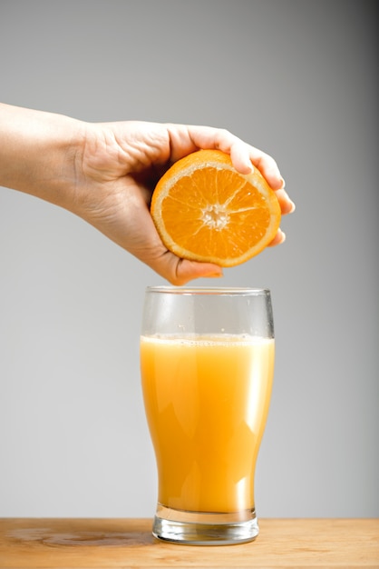 Mão espremendo suco de laranja em vidro