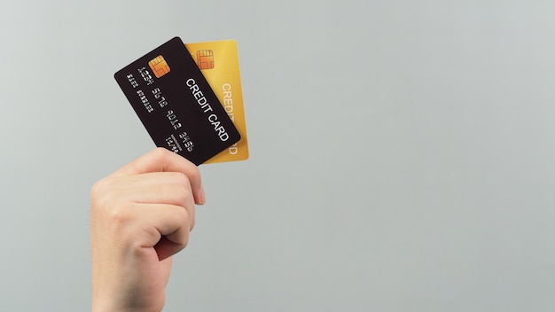 Mão está segurando dois cartões de crédito na cor preta e dourada, isolada no fundo cinza.