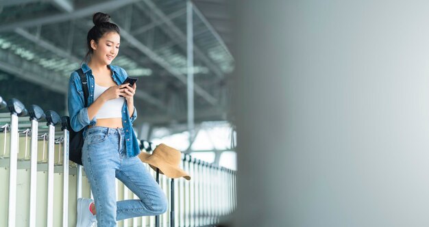 Mão feminina asiática atraente inteligente segure o smartphone verificando a programação do táxi na tela do aplicativo ideias de viagem para cidade inteligente conceptasian feminino use smartphone chamar táxi na estação da plataforma terminal