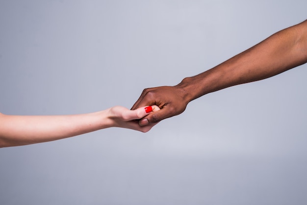 Mão feminina branca branca e mão masculina negra segurando os dedos juntos