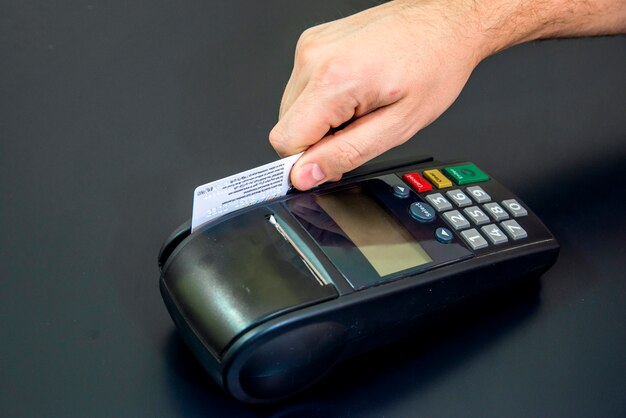 Mão feminina com cartão de crédito e terminal bancário, máquina de cartão ou pos terminal com cartão de crédito em branco branco inserido isolado no fundo preto