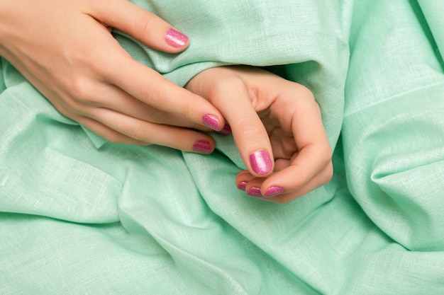 Mão feminina com design de unhas de glitter rosa.