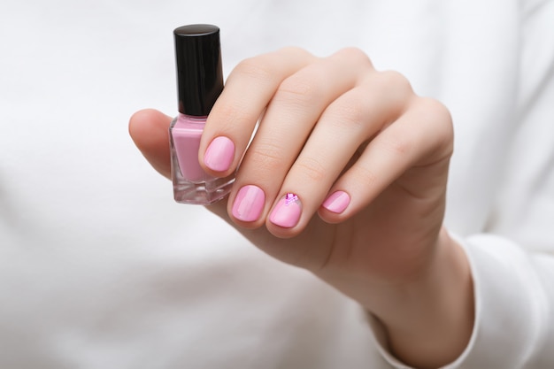 Mão feminina com design de unhas rosa segurando o frasco de esmalte