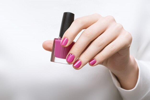 Mão feminina com design de unhas rosa segurando o frasco de esmalte
