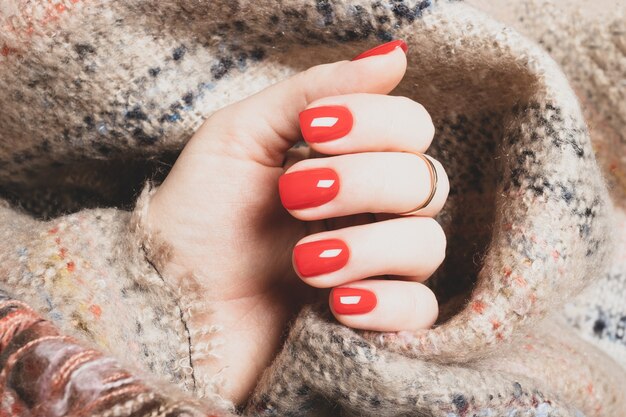 Mão feminina com manicure vermelho brilhante em um fundo de manta de lã marrom