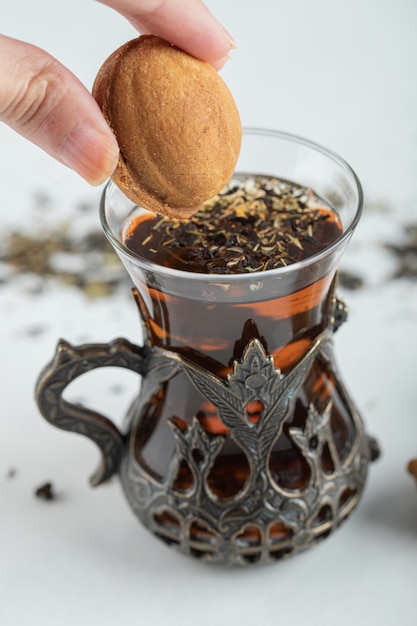 Mão feminina mergulhando um biscoito em forma de noz doce na xícara de chá.