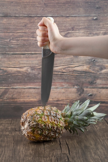 Mão feminina segurando uma faca para cortar abacaxi em fundo de madeira