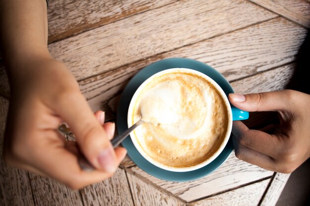 Mão humana segurando a colher de café e mexer o café quente na mesa de madeira
