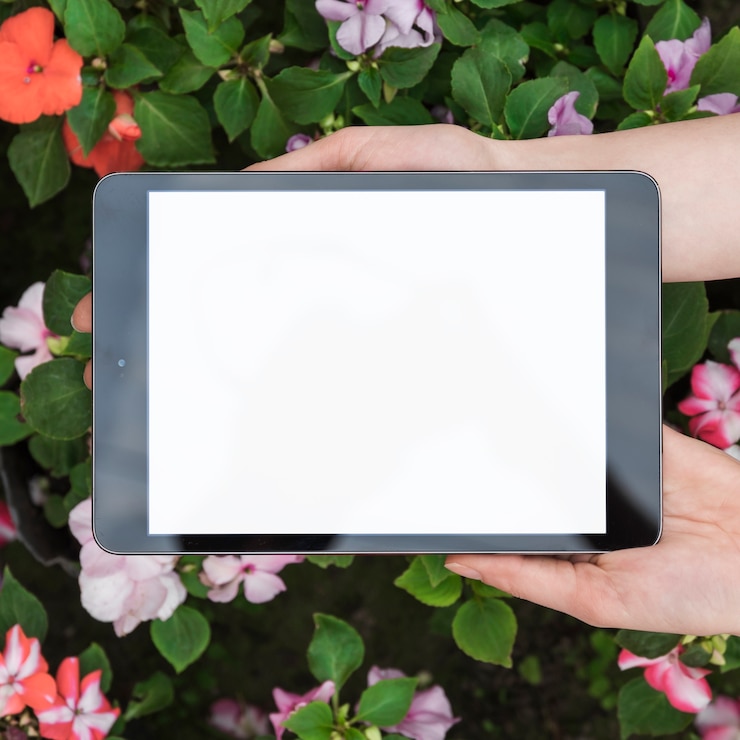 Foto grátis mão humana segurando o tablet digital com tela branca em branco sobre flores frescas