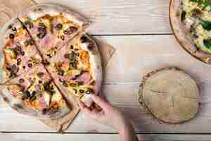 Foto grátis mão humana segurando saboroso cogumelo e bacon pizza na prancha de madeira texturizada