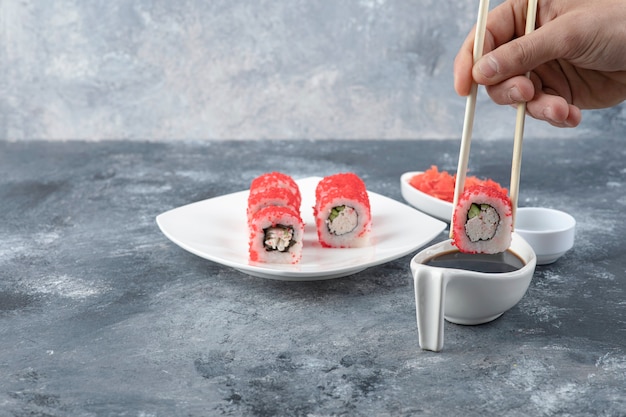 Mão masculina colhendo rolo de sushi com pauzinhos no fundo de mármore