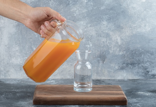 Mão masculina derramando suco de laranja no vidro.