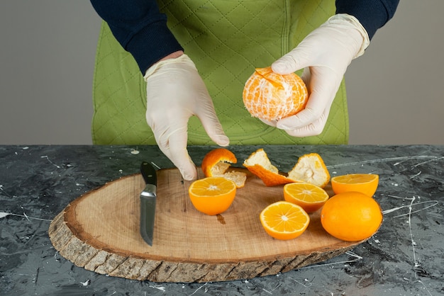 Mão masculina descascando tangerina fresca verde em cima da placa de madeira na mesa.