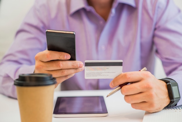 Mão masculina segurando cartão de crédito, desfrutando de compras online na internet usando o tablet de computador digital em casa.