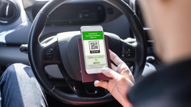 Foto grátis mão masculina segurando passaporte e smartphone com código qr covid-19 do certificado de vacinação internacional em um carro