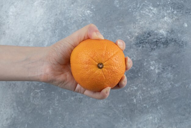 Foto grátis mão masculina segurando uma única laranja na mesa de mármore.