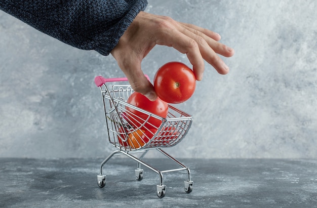 Mão masculina tirando tomate do carrinho de compras