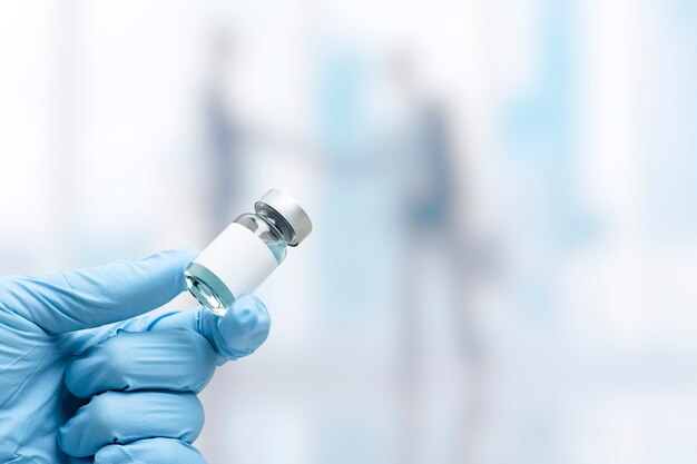 Mão na luva médica segurando um frasco de vacina