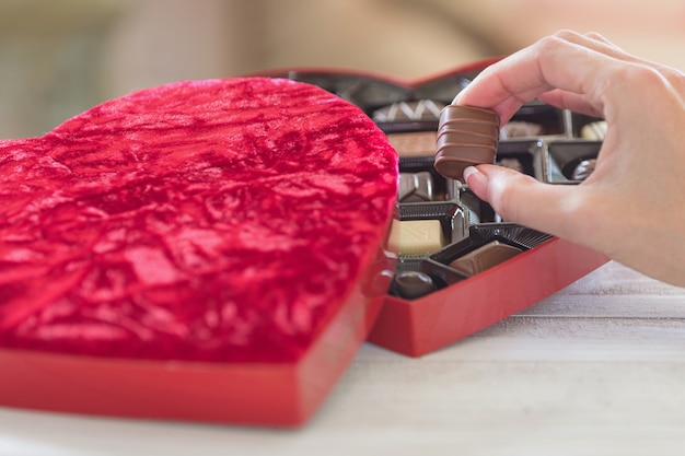 Mão pegando uma trufa de uma caixa de chocolates em forma de coração