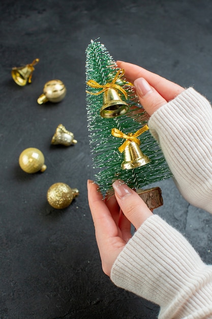 Mão segurando a árvore de Natal e acessórios de decoração em fundo escuro