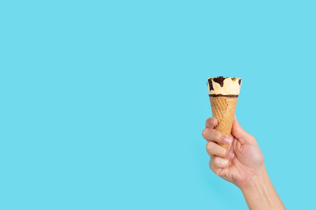 Mão segurando a casquinha de sorvete no fundo azul